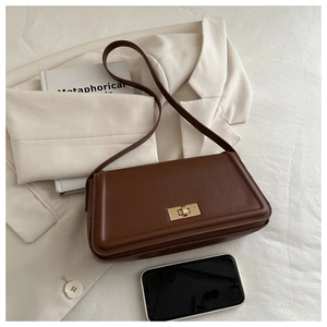Detailed view of dark brown leather tote with golden twist lock on a beige blazer