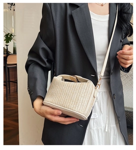 Close-up of straw woven square bag with beige leather trim and metallic strap connector