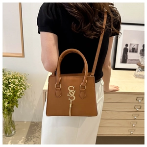 Detail of caramel leather handbag featuring gold SS logo and tassel in a home setting