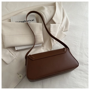 Detail of a brown matte leather shoulder bag on a white blazer with a textured finish