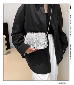 Silver sequin shoulder bag with metal chain strap worn by a model in a stylish setting