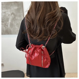 Detail of red drawstring bucket bag with silver chains worn by model on black outfit