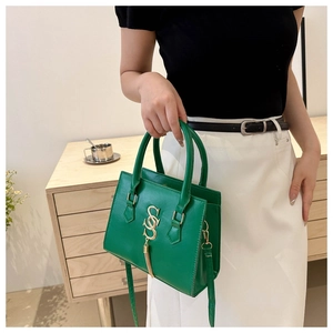 Detail of emerald green textured leather handbag with gold logo and tassel charm