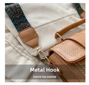 Close-up of golden metal lobster clasp and patterned woven strap on a brown leather bag