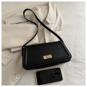 Detail view of black leather tote bag with gold twist lock showing capacity with a smartphone