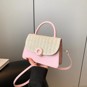 Pink crossbody bag with straw woven flap and golden circular lock held by model