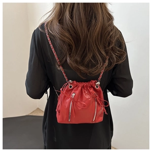 Detail of red leather bucket bag with dual vertical zippers and chain strap on model