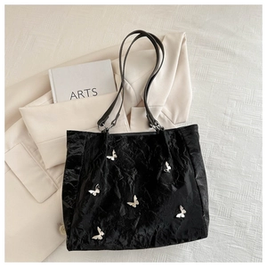 Close-up of black pleated tote bag featuring silver metal butterfly embellishments