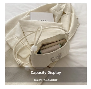Detail view of cream white shoulder bag with silver bow, pearls and interior capacity