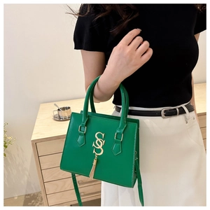 Green square crossbody bag with gold S-pendant and tassel shown on model indoors