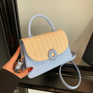 Light blue crossbody bag with woven flap detail and round buckle held by hand