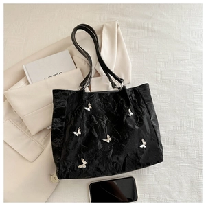 Detail view of black textured bucket bag featuring silver butterfly hardware and slim straps