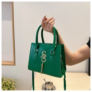 Detail of emerald green handbag with golden double S logo and metallic fringe pendant