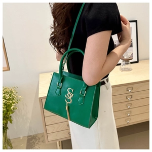 Detail of green leather handbag with gold SSS tassel buckle shown in lifestyle setting