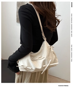 Detail of cream crossbody bag featuring bow accents and a trendy crescent shape