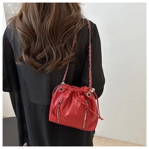 Detail of red drawstring bucket backpack with metal zippers and chain strap on model