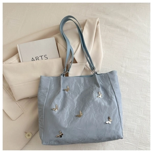 Detail of light blue bucket bag featuring metallic butterfly accents and pleated texture