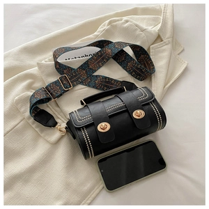 Macro view of black cylindrical handbag with gold studs and vintage pattern strap