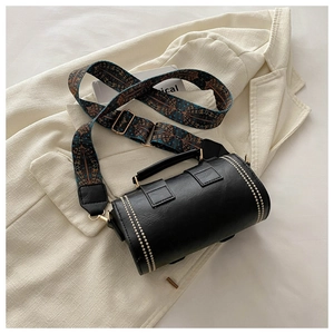 Detail of black leather barrel bag with ethnic woven strap and golden rivet accents