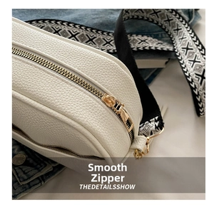 Detail of smooth gold zipper and white lychee texture leather with geometric strap
