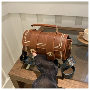 Detail view of brown cylinder bag with white stitching and ethnic print strap