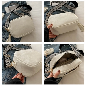 Detail view of white pebbled leather bag with embroidered strap and tassel accessory