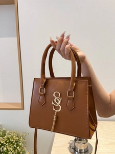 Chic caramel brown leather handbag with gold S logo and tassels on a minimalist background