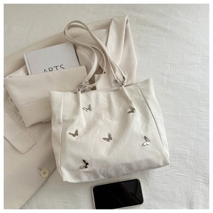 Detail view of cream bucket bag featuring silver 3D metal butterfly charms on glossy leather