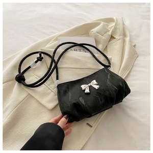 Detail of black pleated shoulder bag featuring a silver metal bow and rope strap knots