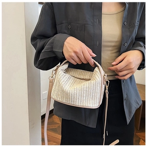 Detail of a woven straw crossbody bag with leather handles shown on a model's arm