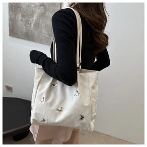 Close-up of off-white bucket bag with silver butterfly charms and pleated texture
