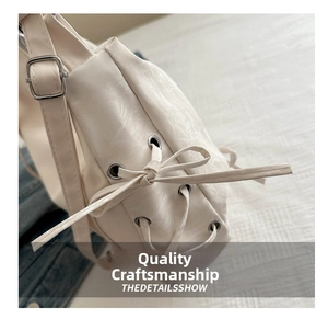 Detail showing creamy white faux leather bag with side bow drawstring and silver eyelet