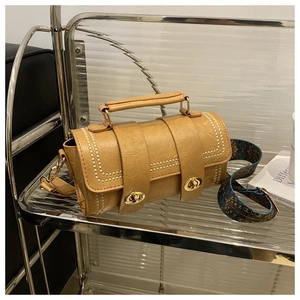 Detail of camel cylinder bag with gold turn-locks, rivets and printed fabric strap