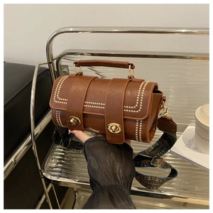 Close-up of vintage brown leather cylinder bag with gold hardware and ethnic strap