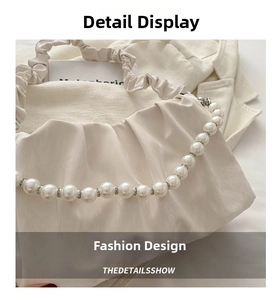 Detail of white pleated cloud bag featuring large pearl handle and soft satin texture
