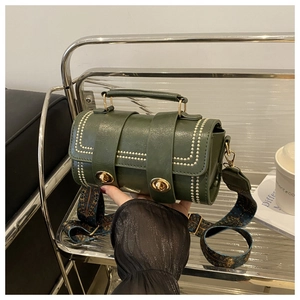 Detail of dark green cylinder bag with gold rivets and embroidered wide shoulder strap