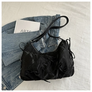 Close-up of black pleated fabric bag with bow accents on a casual denim background