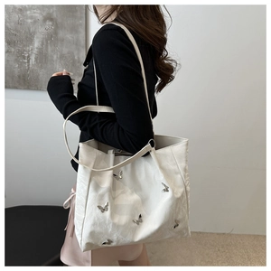Detail of white bucket bag with 3D silver metal butterflies and textured leather