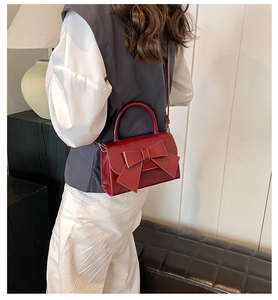 Red patent leather handbag with oversized bow detail being carried by a model