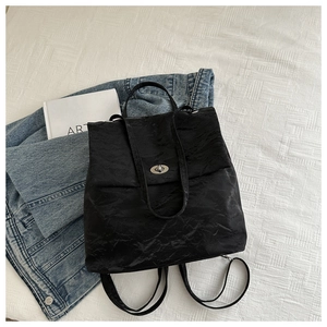 Detailed view of black textured leather bag with silver twist lock on denim background