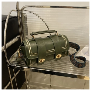 Detail of dark green cylindrical handbag with gold rivets and ethnic woven strap