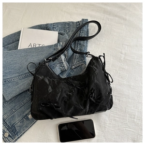 Detail of black pleated shoulder bag featuring elegant bow accents and fabric texture