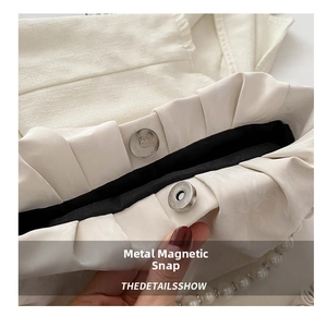Close-up of magnetic snap closure and pearl beads on a white pleated handbag