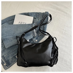 Overhead view of a black bow-tie crossbody bag on a textured background with a denim jacket