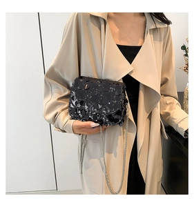 Detail of a chic black sequined crossbody bag with metallic chain on a beige coat
