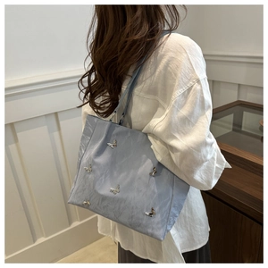 Detailed view of light blue tote bag with silver butterfly charms on a model's shoulder