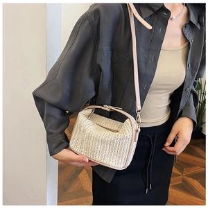 Detail of a beige straw woven crossbody bag styled with a grey oversized shirt and black skirt