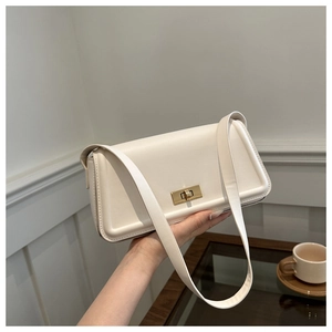 Detail of cream-colored leather baguette bag featuring a gold rotating metal clasp
