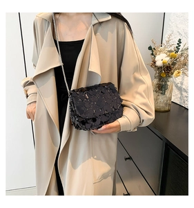 Detail of a chic black sequined crossbody bag with a silver chain on a beige coat