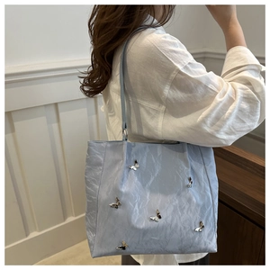 Close-up of light blue bucket bag with pleats and silver butterfly metal ornaments